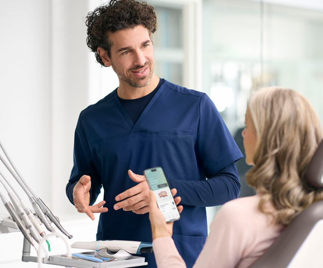 Male dentist and female patient holding phone with 3Shape app displayed.